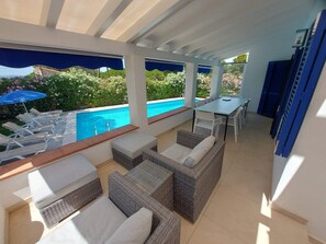 A covered outdoor area with a pool, lounge chairs, wicker furniture, and a table.