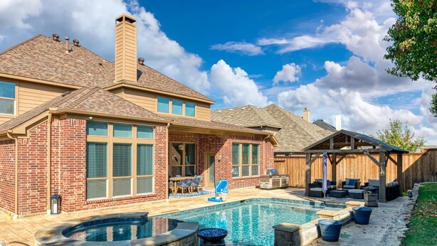 Un jardin avec une piscine, une terrasse couverte et une maison en briques.