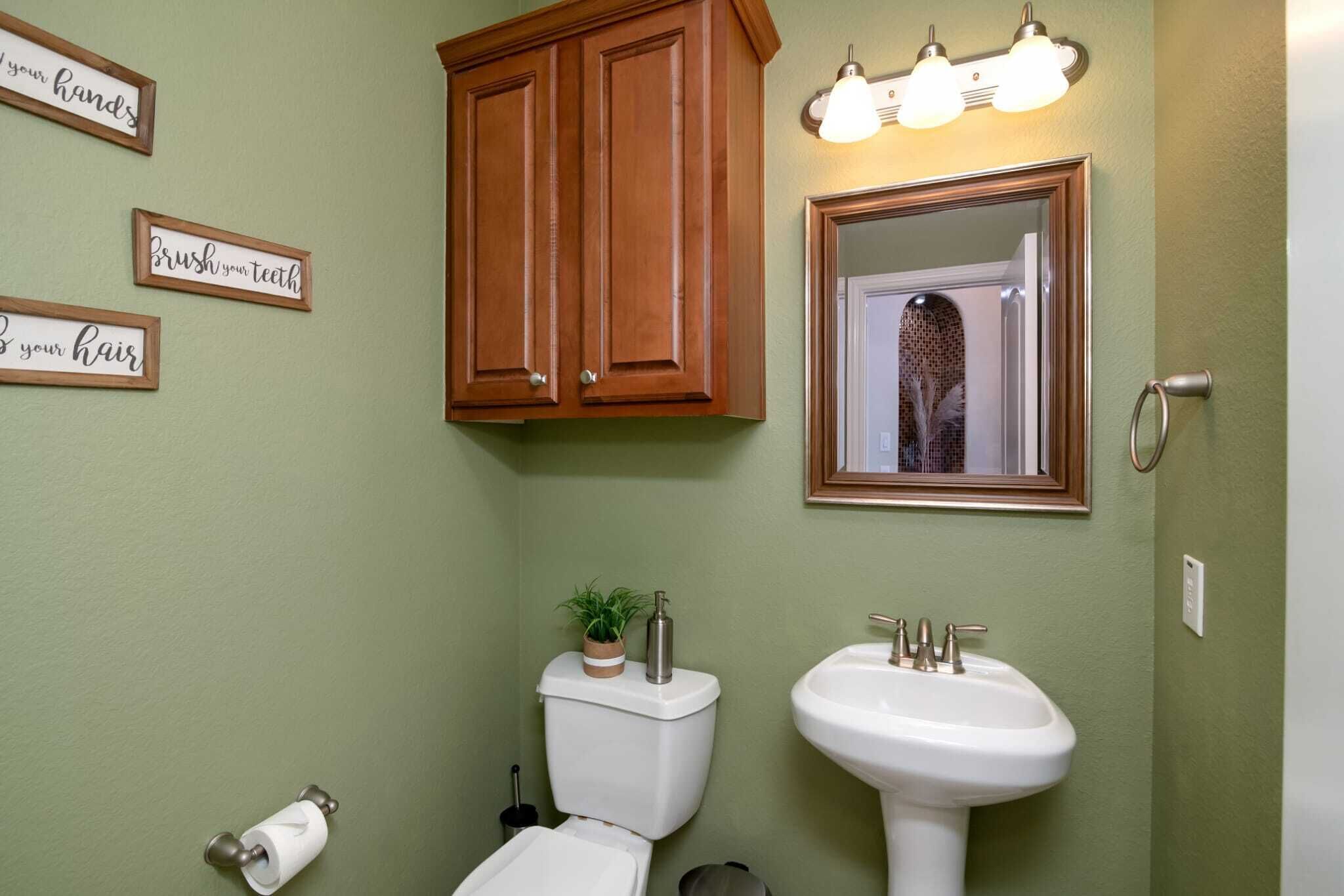 Een badkamer met toilet, wastafel, houten kastjes en drie motiverende borden aan de muur.