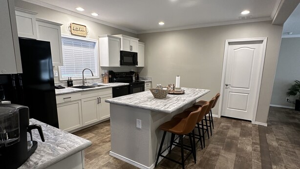 A modern kitchen with white cabinets, a central island with bar stools, a black refrigerator, and a microwave.