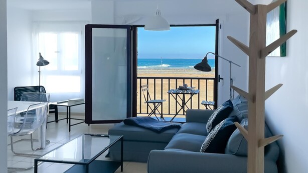 A modern living room with a glass coffee table, a sofa, and a view of the beach. - Adela Homes by Best Holidays Fuerteventura (Corralejo)
