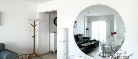 A modern living room with a round mirror reflecting the dining area, a grey sofa, a coffee table, and a vase with dried flowers.
