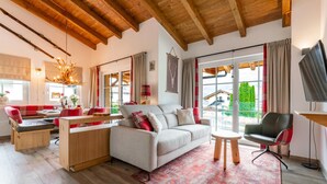 A modern living room with a sofa, a dining table, and a TV. - Penthouse near Kaprun with sauna & stunning views (Piesendorf)