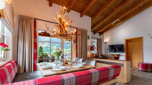 A dining area with a bench, table set for four, and a chandelier. - Penthouse near Kaprun with sauna & stunning views (Piesendorf)
