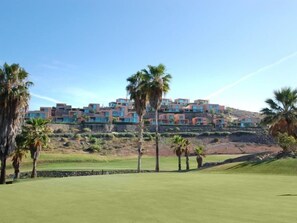 Un campo de golf con edificios modernos de varios pisos al fondo.