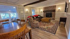 A spacious living room with a fireplace, a dining area with a wooden table and chairs, and a cozy seating area with patterned sofas and a rug. - Renovated home on snowmobile trail, firepit, hot tub, views,10 min from skiing, dogs welcome! (Twin Mountain)
