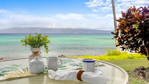 A table with a white tablecloth, a white vase with green leaves, two white mugs, and a white napkin with a brown bracelet. - Whale Watching from your lanai, unbeatable views (Lahaina)