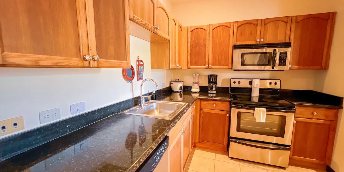 Una cocina con armarios de madera, un microondas de acero inoxidable, una estufa y un lavamanos.