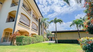 Um edifício com várias andares, varandas, um gramado bem cuidado e palmeiras.