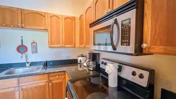 A kitchen with wooden cabinets, a stainless steel sink, a microwave, a stove, and a coffee maker.