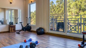 Habitación amplia con un ventanal grande que ofrece vistas a un bosque. Contiene equipo de ejercicio como una bicicleta estática, pesas y una colchoneta de yoga.