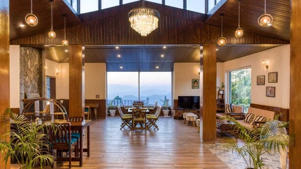 Una habitación amplia con suelo de madera, un candelabro, una zona de comedor con mesa y sillas, un conjunto de sofás y un televisor.