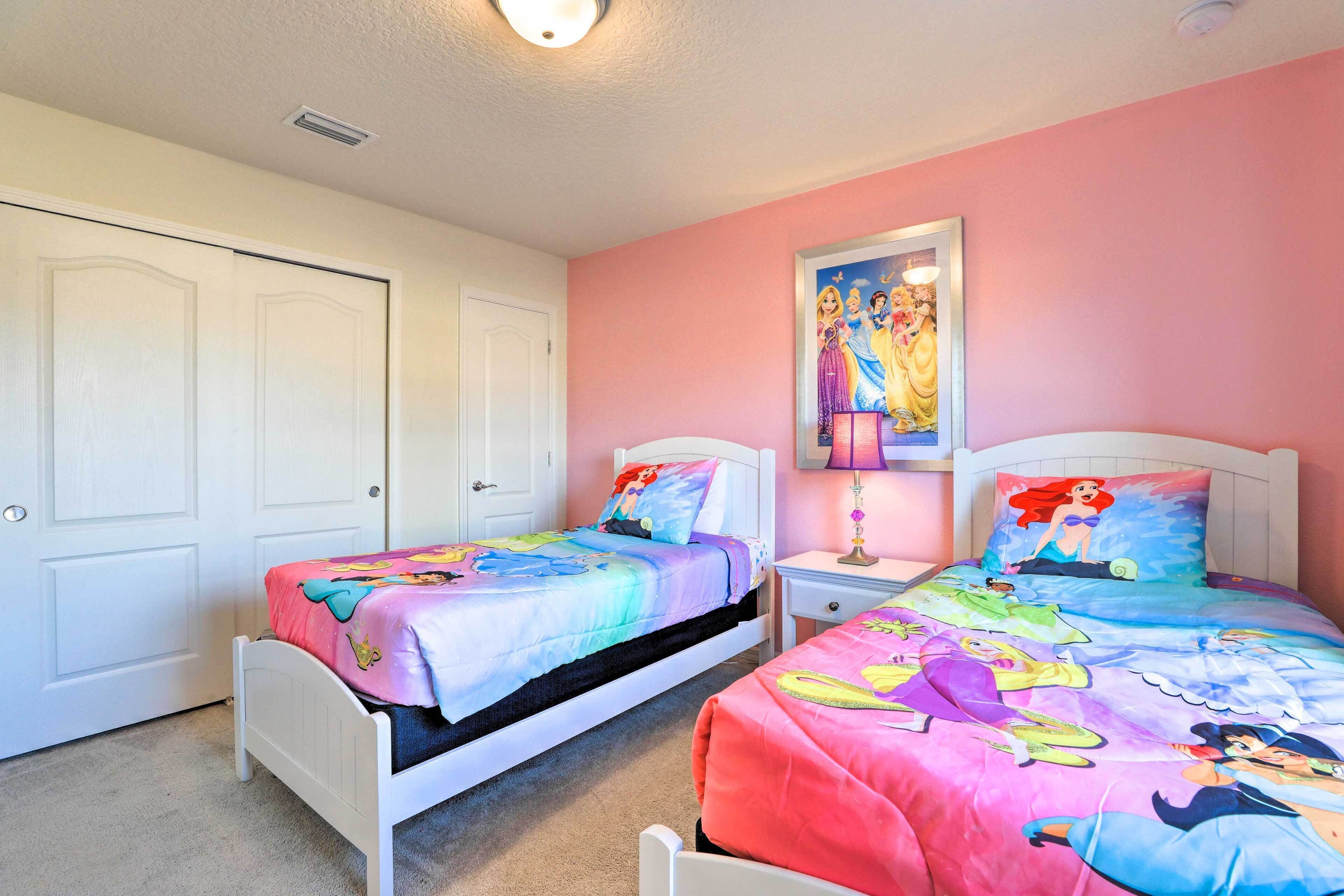 A bedroom with two beds, each with a Disney-themed bedspread, a nightstand with a lamp, and a poster on the wall.
