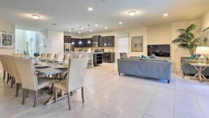 A spacious living room with a grey sofa, dining area with chairs, and a kitchen in the background. - Upscale Kissimmee Retreat (Kissimmee)