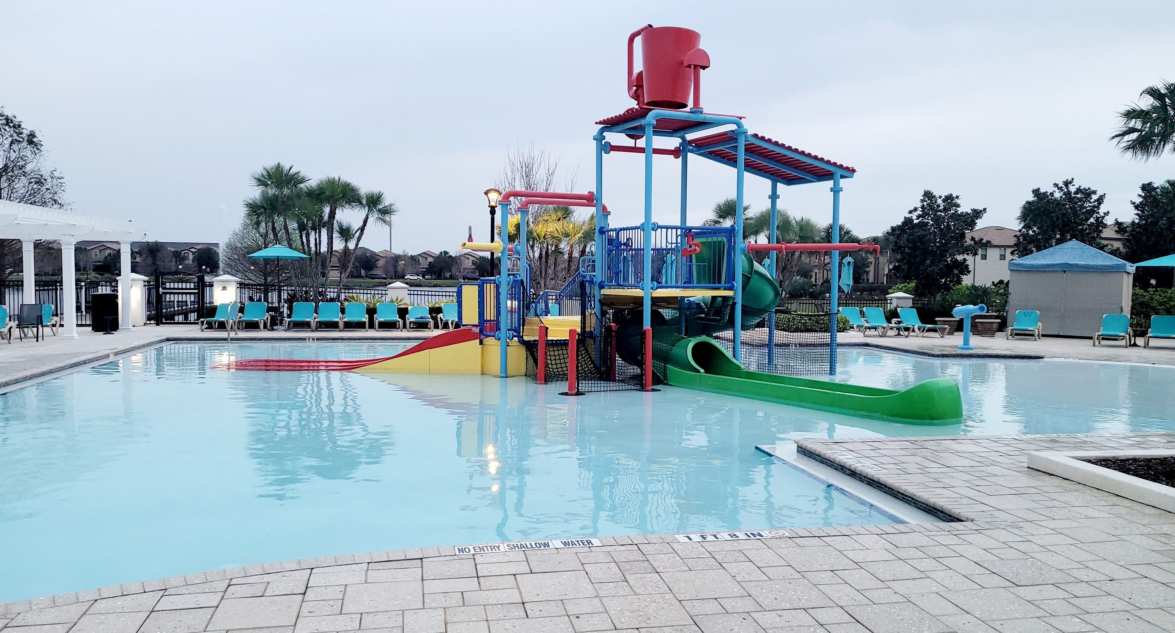 A pool area with a water play structure, lounge chairs, and a covered seating area.