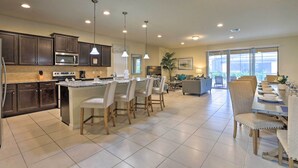 A modern kitchen with dark cabinets, a central island with bar stools, and a dining area with a large table and chairs. - Upscale Kissimmee Retreat (Kissimmee)
