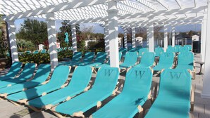 A row of turquoise sun loungers under a white pergola with a view of the pool area. - Upscale Kissimmee Retreat (Kissimmee)