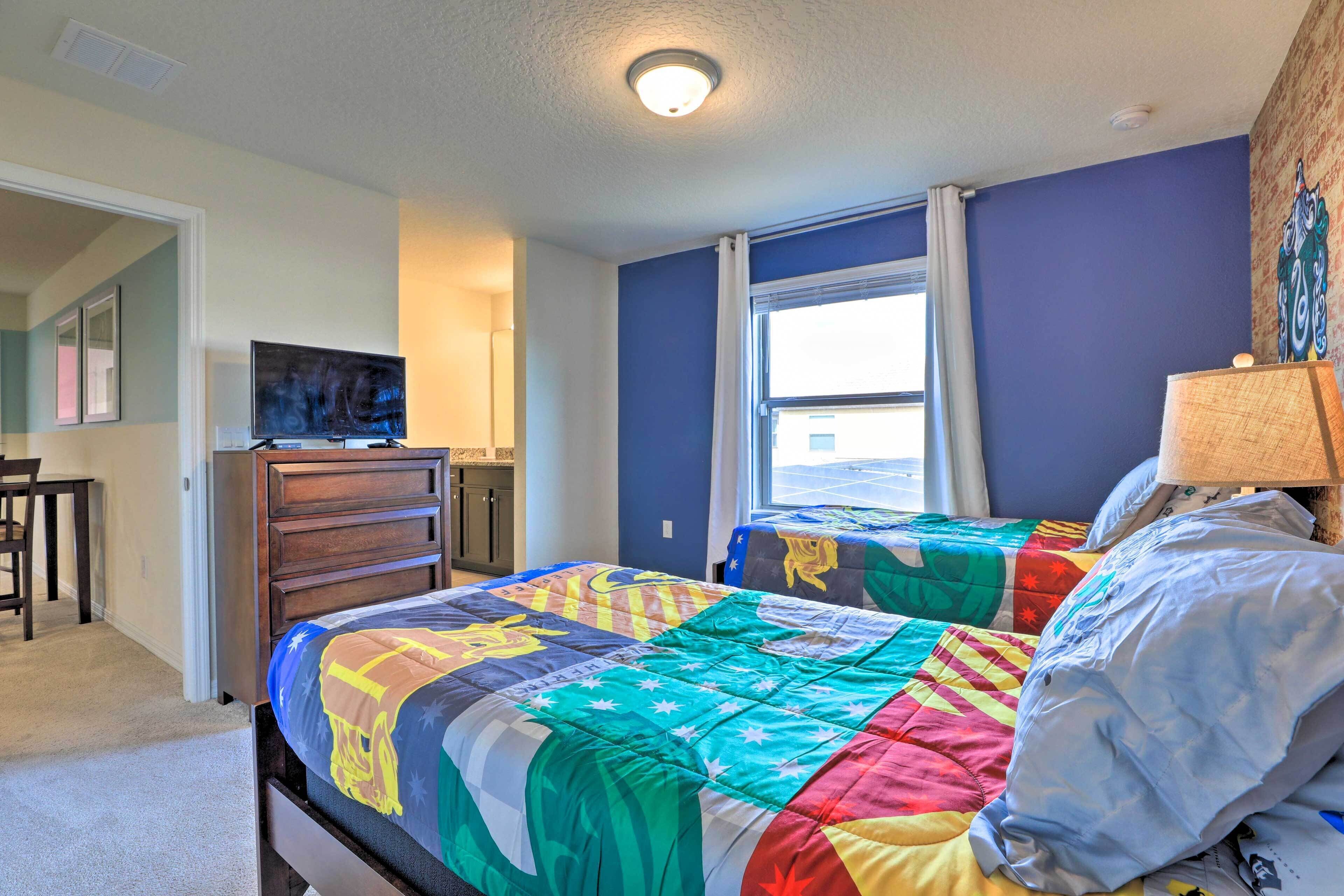A bedroom with a large bed, a dresser, a television, and a window with curtains.