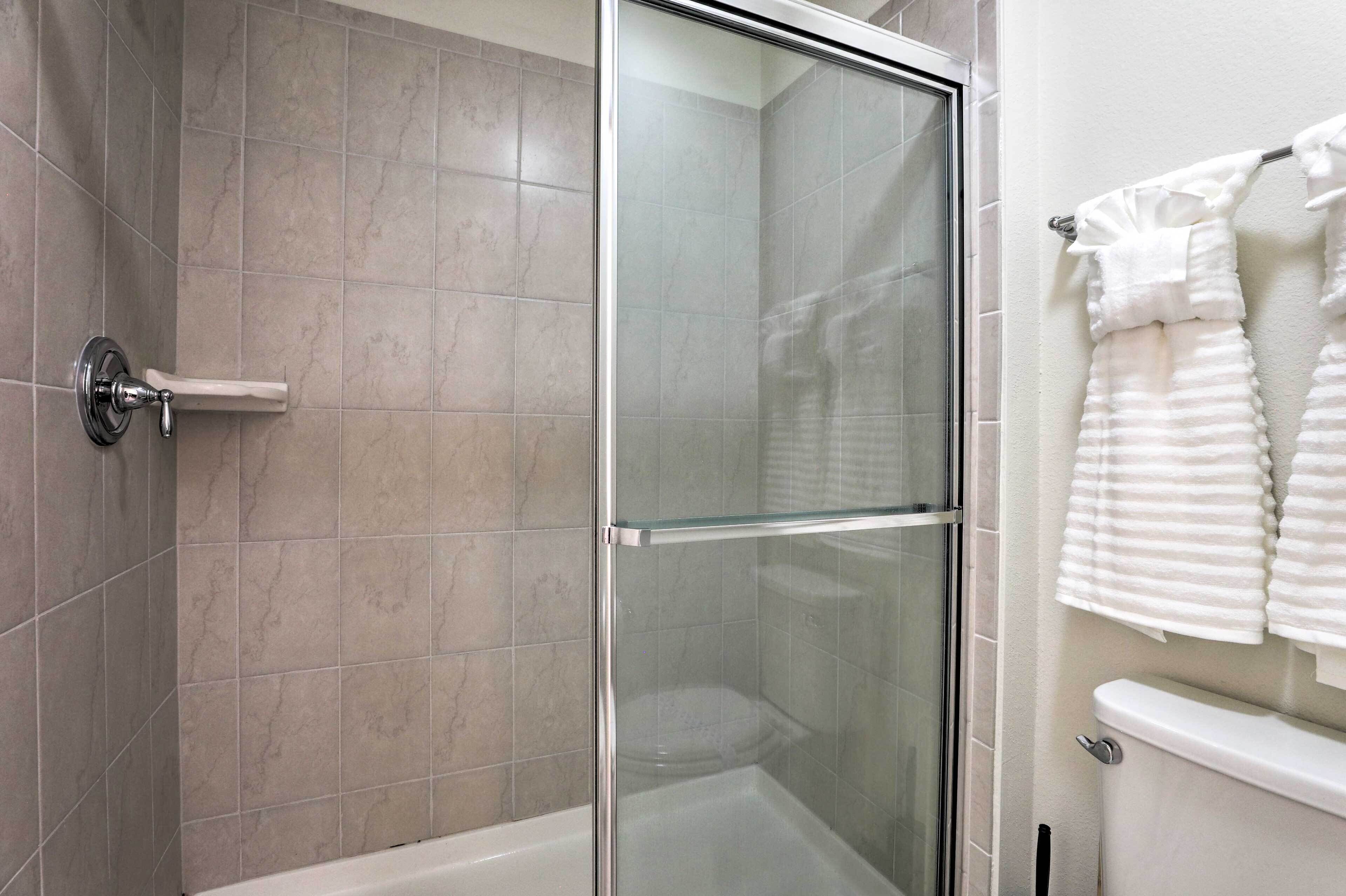 A modern bathroom with a glass-enclosed shower, a toilet, and a towel rack with folded towels.