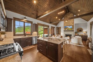 A spacious kitchen with a large island, wooden ceiling beams, and a stone fireplace.