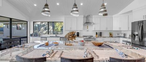 A modern kitchen with white cabinets, a central island with stools, pendant lighting, and a large window providing natural light.