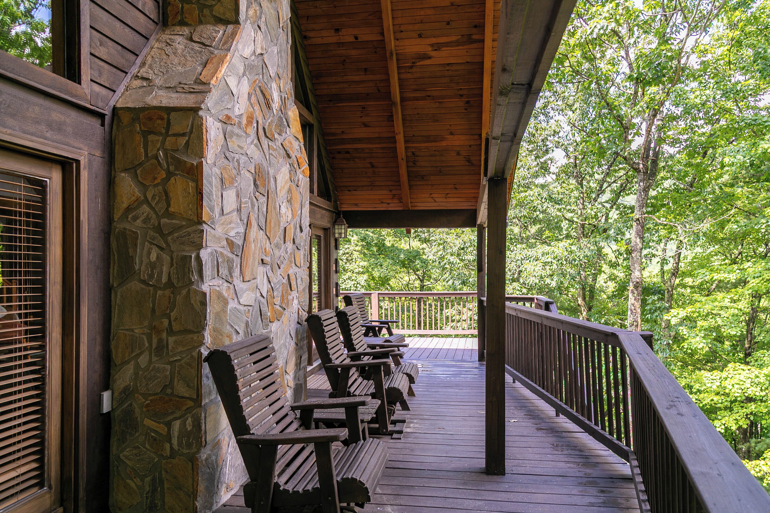 A covered wooden deck with stone walls, benches, and a railing overlooking a forested area.