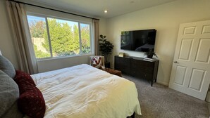 A bedroom with a large bed, a dresser, a TV, and a window with a view of trees. - New 3B Home / near Sequoia, EV, +More (Visalia)
