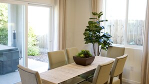 A dining area with a glass table, six chairs, a potted plant, and a view of the outdoors through large windows. - New 3B Home / near Sequoia, EV, +More (Visalia)