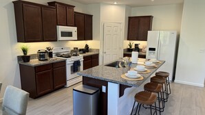 A modern kitchen with dark wood cabinets, a white stove, a built-in microwave, and a refrigerator. - New 3B Home / near Sequoia, EV, +More (Visalia)