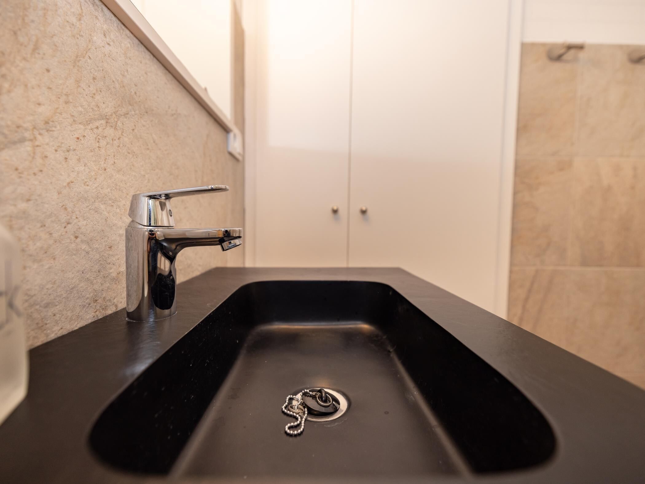 Un baño moderno con un lavabo negro, grifo cromado y una puerta individual al fondo.