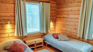A cabin-style room with two single beds, a small table, and a window with curtains.