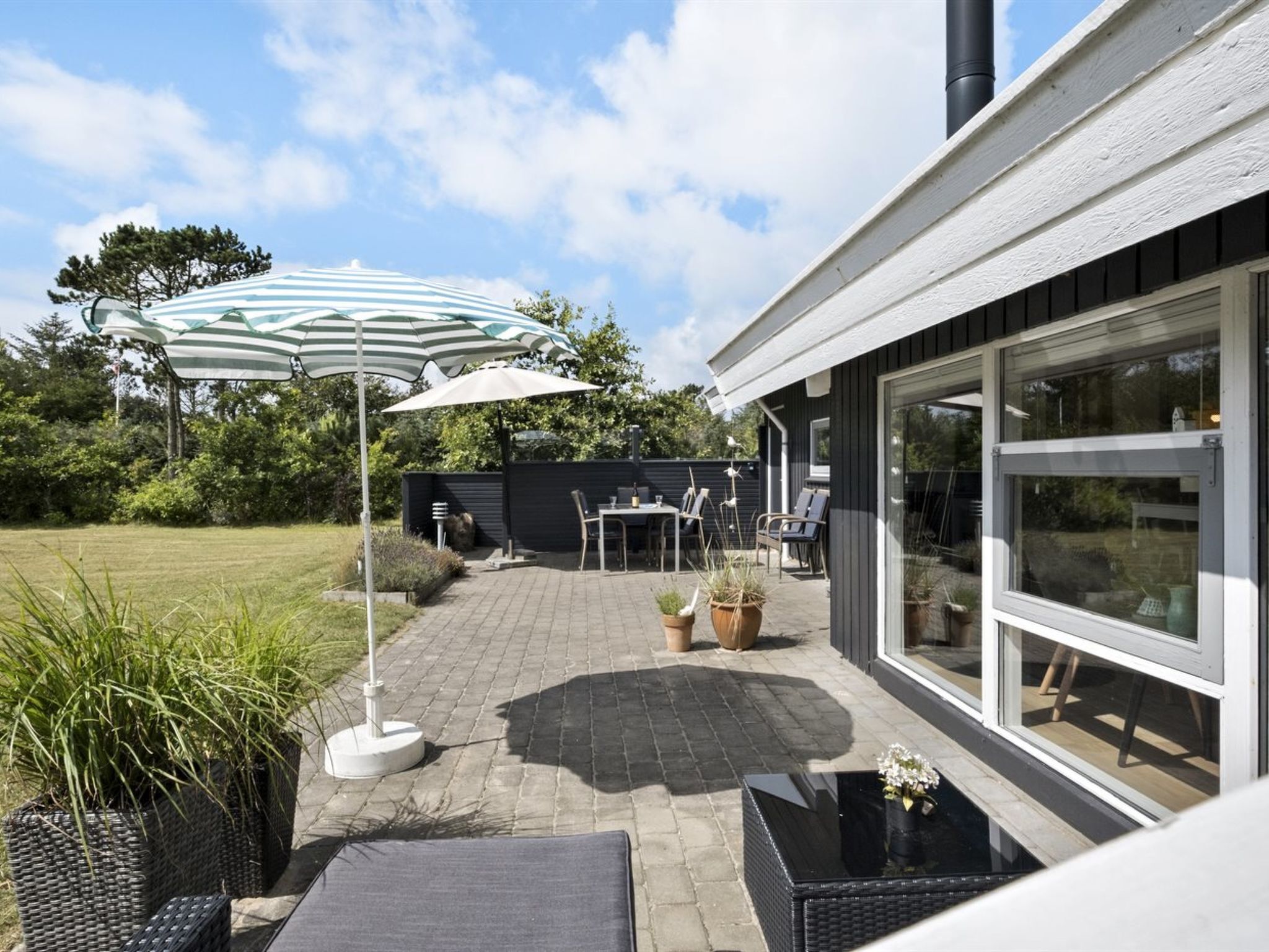 A patio area with outdoor furniture, a striped umbrella, and potted plants.
