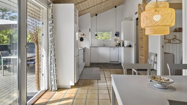 Een moderne keuken met witte kasten, een eethoek met een witte tafel en een groot raam met uitzicht op het landschap.
