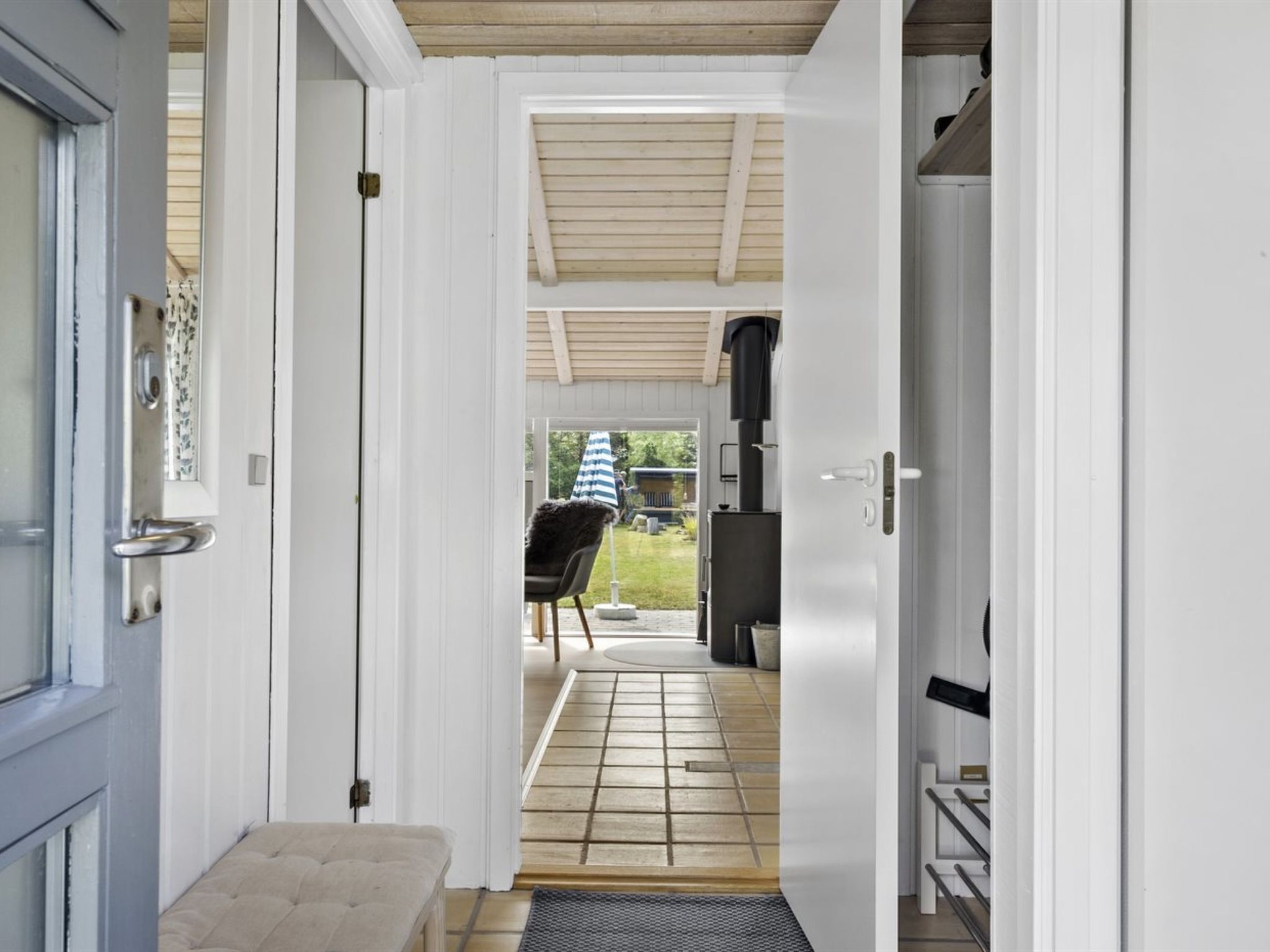 A corridor leading to an outdoor patio with a grill, a bench, and a chair.