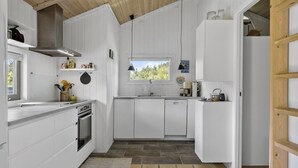 Een moderne keuken met witte kastjes, een houten plafond, een raam en een betegelde vloer.