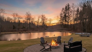 A lakeside outdoor seating area with a fire pit and Adirondack chairs.