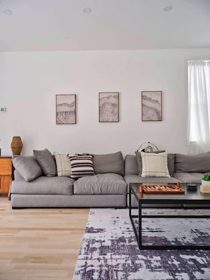 Un salon moderne avec un canapé gris, une table basse et trois œuvres d’art encadrées accrochées au mur.