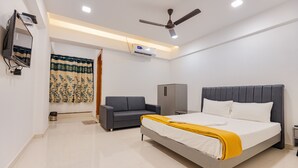 A modern bedroom with a bed, a grey sofa, a wardrobe, and a ceiling fan. - Hotel Lennox Best In surat (Surat)