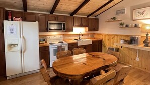 Une cuisine avec des meubles de rangement en bois, un réfrigérateur blanc, un four à micro-ondes, une cuisinière et une table à manger en bois avec des chaises.