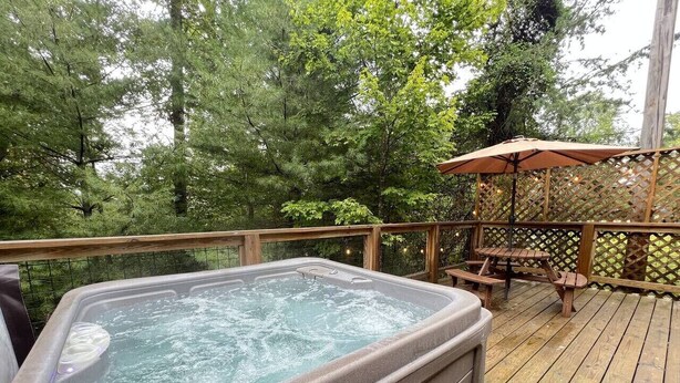 Un bain à remous sur une terrasse en bois, entouré d’arbres.