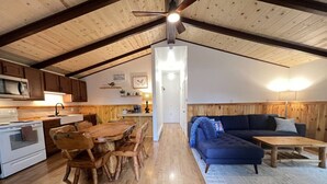 Un intérieur rustique avec une table et des chaises en bois, un canapé bleu et une cuisine dotée de meubles en bois et d’un four à micro-ondes.