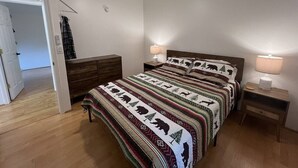 Une chambre à coucher comprenant un lit, deux tables de chevet, un ventilateur de plafond et une porte donnant sur une autre pièce.
