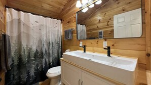 Une salle de bain rustique, avec des murs en bois, une grande fenêtre, un lavabo blanc et des toilettes.