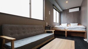 A modern hotel room with a sofa, a bed, a wooden table, and large windows. - BESTIE - DOYANEN HOTELS (Osaka)