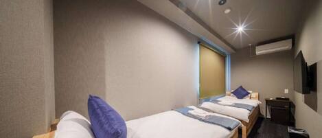 A hotel room with three single beds, a desk, a chair, a TV, and an air conditioning unit.