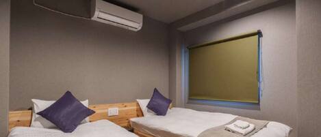 A room with two single beds, a window with blinds, an air conditioning unit, and a wooden headboard.