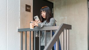 A person standing on a balcony, holding a smartphone and a coffee cup. - BESTIE - DOYANEN HOTELS (Osaka)