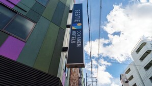 A hotel sign with the name 'BESTIE DOYANEN HOTELS' against a backdrop of a building with a green and purple facade. - BESTIE - DOYANEN HOTELS (Osaka)