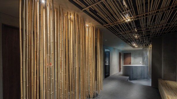 A modern interior with a bamboo wall, a concrete reception desk, and a wooden bench. - BESTIE - DOYANEN HOTELS (Osaka)