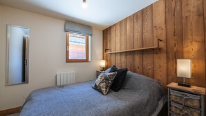 Un dormitorio con una cama grande, paneles de madera en las paredes, una ventana, un radiador y lámparas de noche.